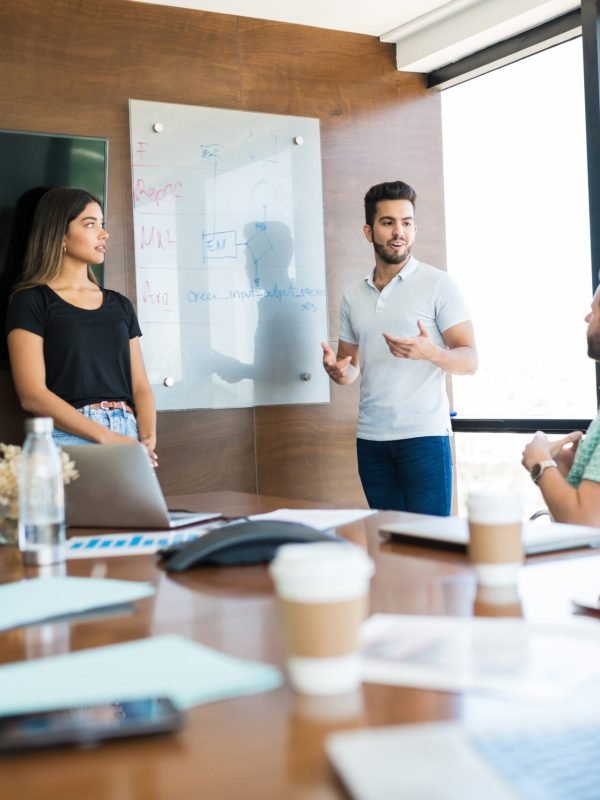 Confident young coworkers explaining strategy to colleagues in meeting room at coworking office
