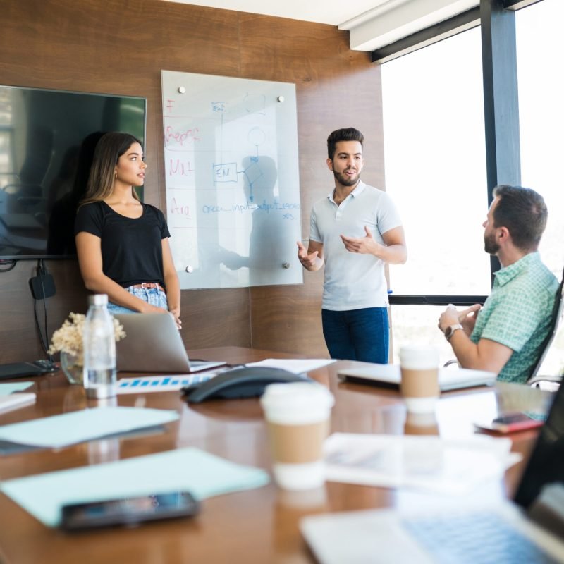 Confident young coworkers explaining strategy to colleagues in meeting room at coworking office
