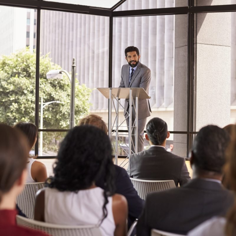 Hispanic man presenting business seminar leaning on lectern